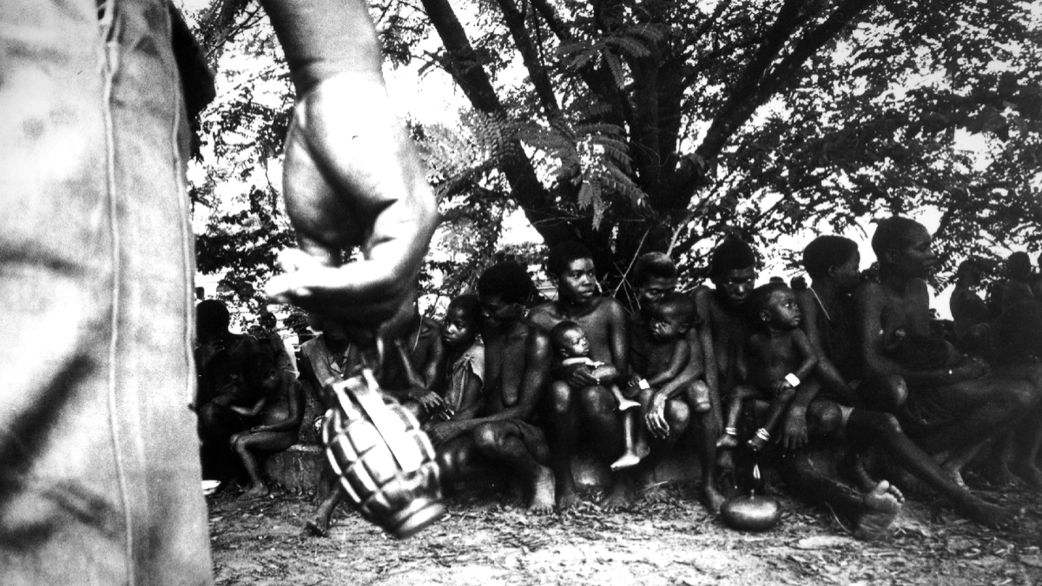 A federal soldier swings a hand grenade by its release pin while guarding Ibo women prisoners and their children in Nigeria, during the Biafran War. [Getty Images]