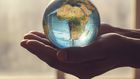 Deux mains tendues, tenant délicatement une petite plante qui pousse au centre d'un globe terrestre.