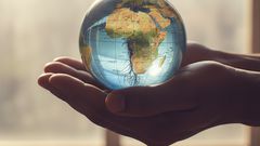 Deux mains tendues, tenant délicatement une petite plante qui pousse au centre d'un globe terrestre.