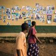 A man and a woman walk past a wall covered with electoral posters in Beni on December 21, 2018