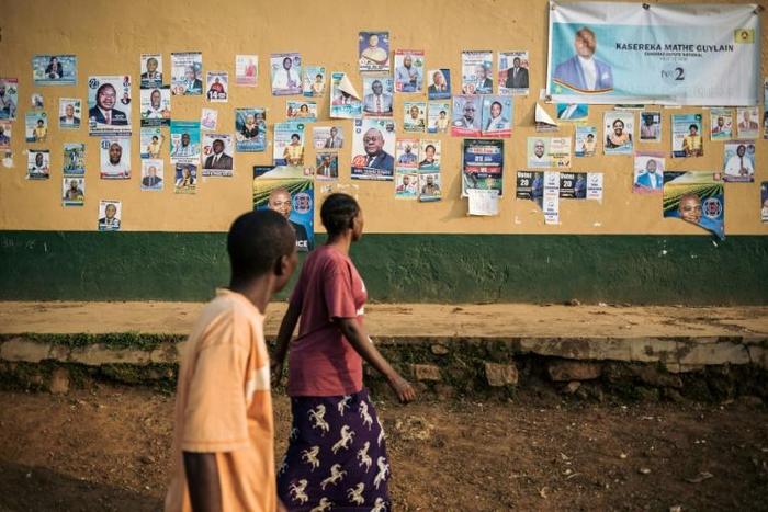 A man and a woman walk past a wall covered with electoral posters in Beni on December 21, 2018