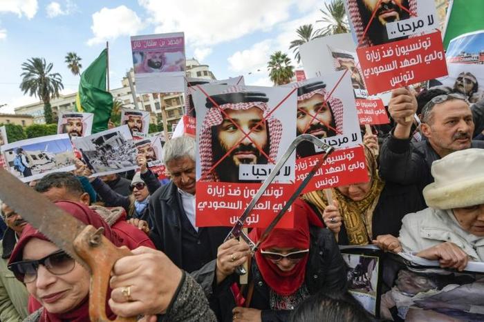 Tunisian women hold up saws and signs saying in Arabic, "No welcome, Tunisians against the visit of the Saudi Crown Prince to Tunisia", during an anti-Saudi Crown Prince protest in Tunis on November 27, 2018
