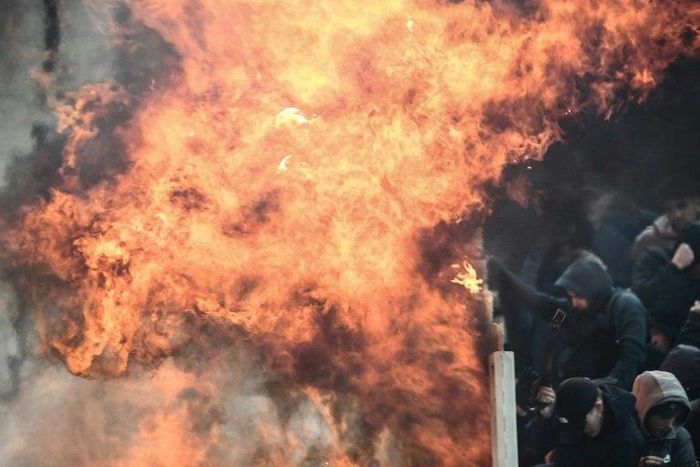 Ajax fans shelter from the flames of a Molotov cocktail at the Athens Olympic Stadium