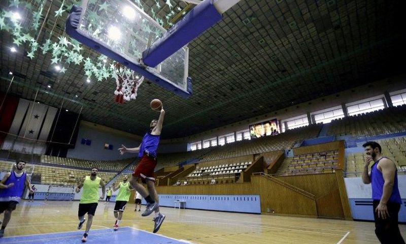 Syrian basketball team players take part in a training session at a stadium decorated with portraits of Syrian President Bashar al-Assad and his late father Hafez al-Assad (top R)