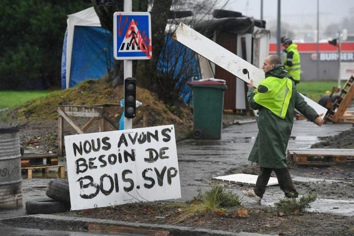 One of the 'yellow vest' protesters helps the construction work at a roundabout in Brest, western France. The sign next to him reads '"We need more wood, please'.