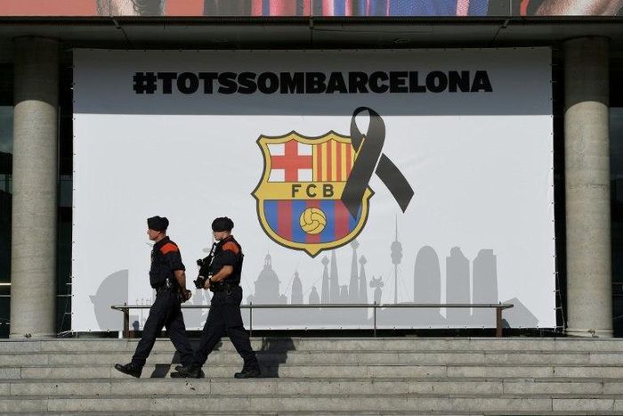 Armed Catalan policemen pass by the FC Barcelona logo with a black ribbon and a message reading, "We are all Barcelona" at the Camp Nou stadium in Barcelona on August 20, 2017
