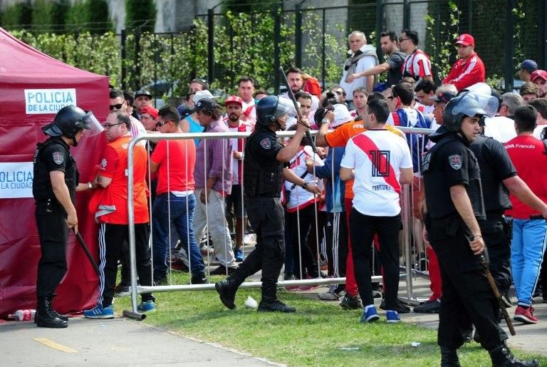 Police officers and River Plate fans wait at a gate of the the Monumental stadium ahead of the "superclasico" Copa Libertadores final against arch rivals Boca Juniors