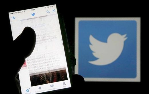 A man reads tweets on his phone in front of a displayed Twitter logo in Bordeaux, southwestern France, March 10, 2016. REUTERS/Regis Duvignau/Illustration/File Photo