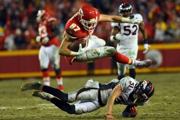 Tight end Travis Kelce of the Kansas City Chiefs leaps over free safety Justin Simmons of the Denver Broncos during their game at Arrowhead Stadium in Kansas City, Missouri, on December 25, 2016
