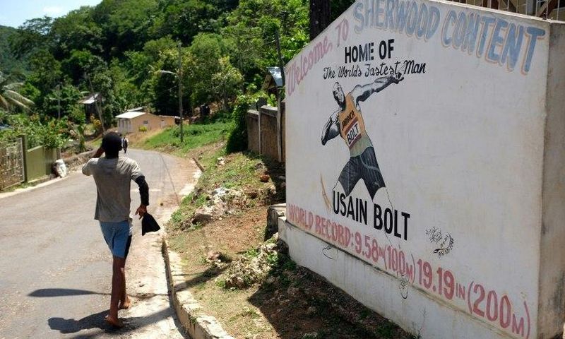 A boy walks past a welcome sign depicting Jamaican sprinter Usain Bolt at an intersection in his hometown of Sherwood Content, Jamaica