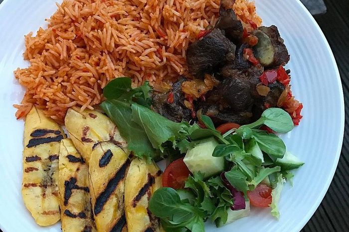 Coconut jollof rice, served with fried goat meat, grilled plantain and some leafy vegetables (Foodace)
