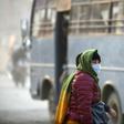 A woman covers her face with a mask as she walks along a dusty road in Kathmandu