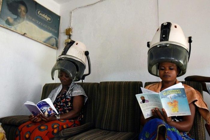 Women sitting under hair steamers read books from a mini-library at a hairdresser's in Abidjan.