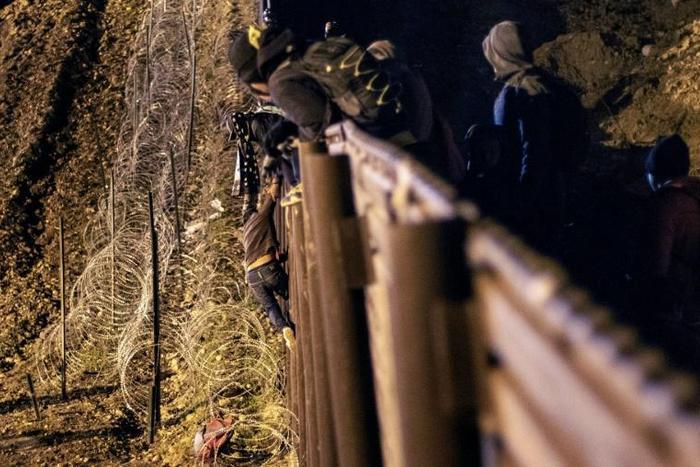A Central American migrant scales the US-Mexico border fence from Tijuana, Mexico, into the US (L) on January 1, 2019