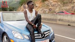 Shatta Wale sitting on a car