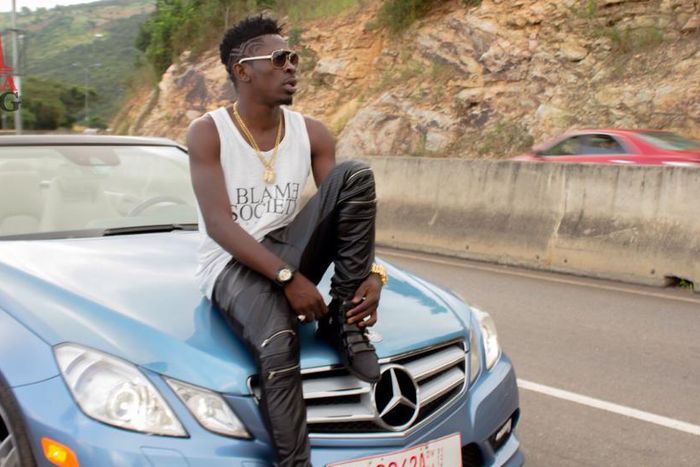 Shatta Wale sitting on a car