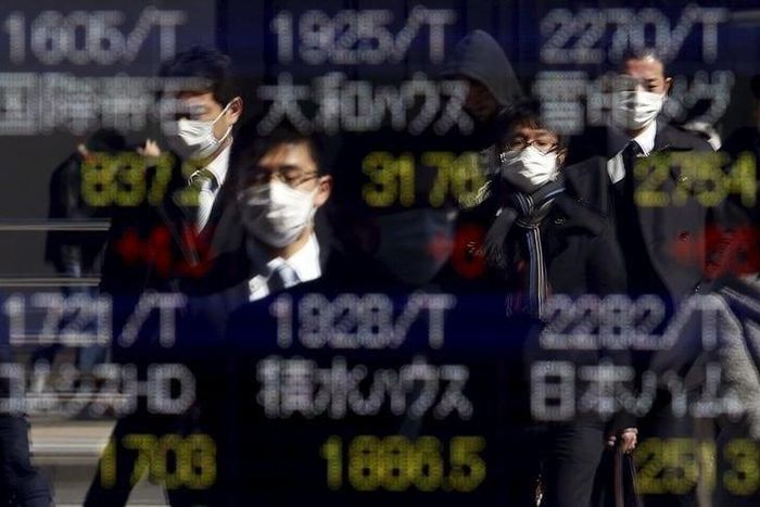 Pedestrians wearing masks are reflected in an electronic board showing various stock prices outside a brokerage in Tokyo, Japan, February 26, 2016.