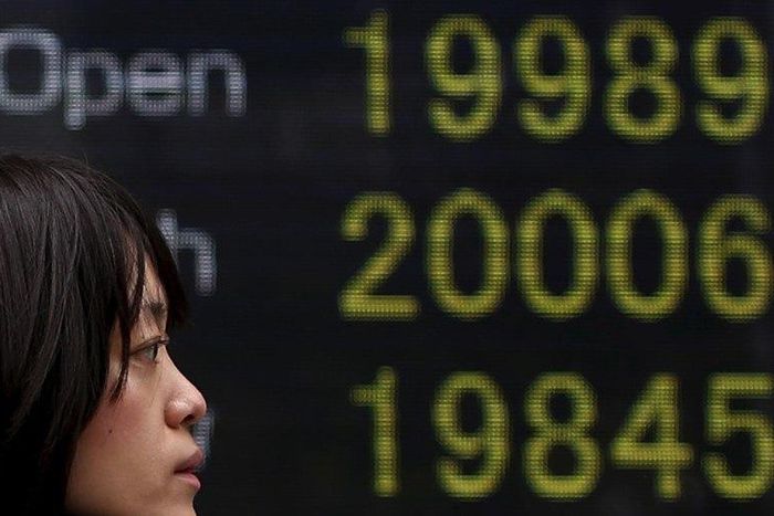 A pedestrian walks past an electronic board showing the Japan's Nikkei averages (from top current rate,daily high, and daily low) outside a brokerage in Tokyo April 10, 2015. REUTERS/Yuya Shino