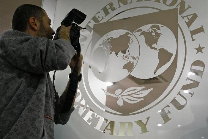 A photographer takes pictures through a glass carrying the International Monetary Fund (IMF) logo during a news conference in Bucharest March 25, 2009.  REUTERS/Bogdan Cristel