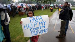 A woman holds a banner written "Papa Help My Country Burundi" before a mass by Pope Francis, as rain falls in Kenya"s capital Nairobi, November 26, 2015.