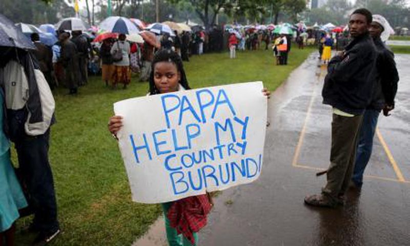 A woman holds a banner written "Papa Help My Country Burundi" before a mass by Pope Francis, as rain falls in Kenya"s capital Nairobi, November 26, 2015.