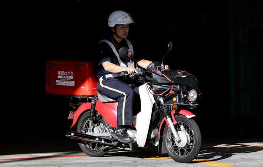 A mail carrier rides a motorcycle as he departs from a Japan Post post office in Tokyo.