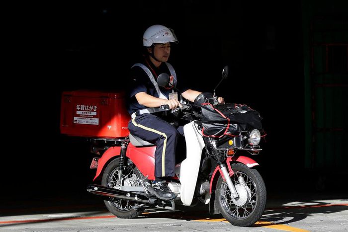 A mail carrier rides a motorcycle as he departs from a Japan Post post office in Tokyo.