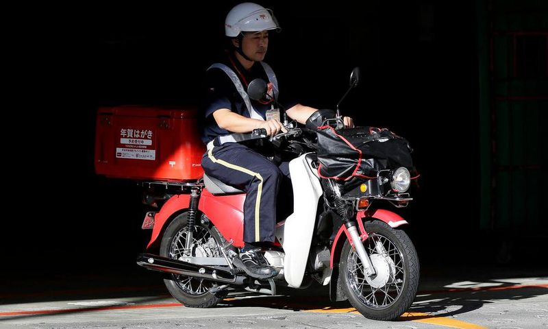A mail carrier rides a motorcycle as he departs from a Japan Post post office in Tokyo.