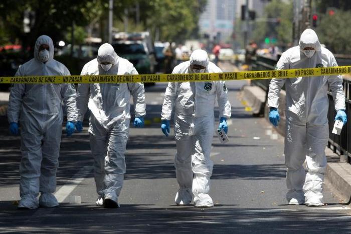 Police bomb squad personnel inspect the scene after a blast at a bus stop injured at least four people in downtown Santiago