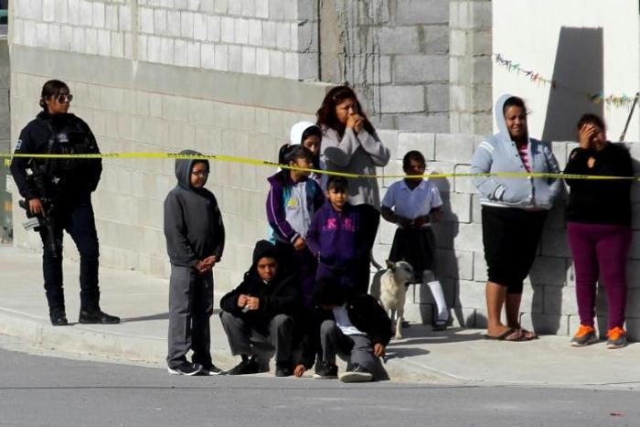 A police officer (L) and neighbors watch a house where five people were killed in Mexico's Ciudad Juarez on January 16, 2019 -- the country suffered a record 33,341 homicides in 2018