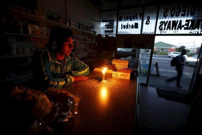 A shopkeeper waits for customers in his candlelit  fast food store during a load shedding electricity blackout in Cape Town April 15, 2015.       REUTERS/Mike Hutchings