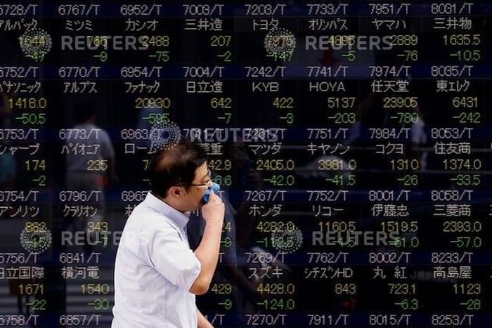 A man walks past a display showing stock prices in Tokyo August 12, 2015. REUTERS/Thomas Peter