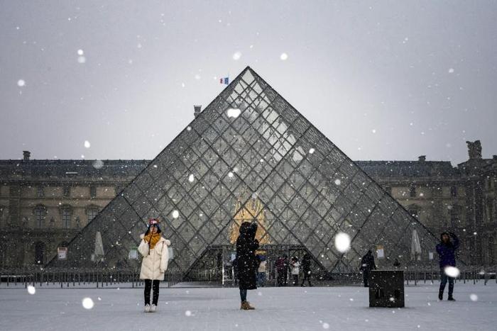 Tourists take pictures at the Louvre Pyramid as the snow falls over Paris