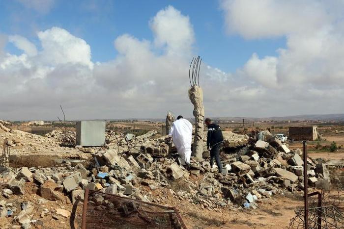 Libyan men walk amidst debris of a destroyed building in the town of Al-Goualiche, 120 kilometres (75 miles) west of the capital Tripoli