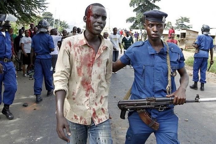 A riot policeman escorts an injured protester who was hit during clashes with riot police against the decision to allow President Pierre Nkurunziza to run for the country's third term presidency seat.