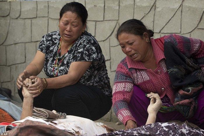 Grieving women hold the hands of relatives as they lie beneath a thin white sheet in the city of Kathmandu.