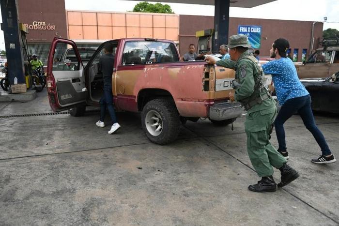 People push a vehicle up to the pump to fill up on gas at a station in Acarigua in Venezuela, which has started rationing fuel