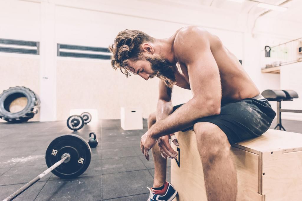 Exhausted male cross trainer taking a break from weightlifting in gym