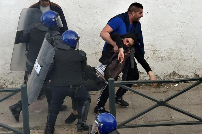 Algerian security forces drag a man away as they respond to protests in the capital Algiers on Friday