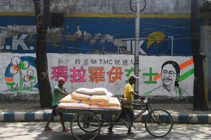 Delivery men walk past a mural bearing Chinese characters in support of a Trinamool Congress candidate in Kolkata