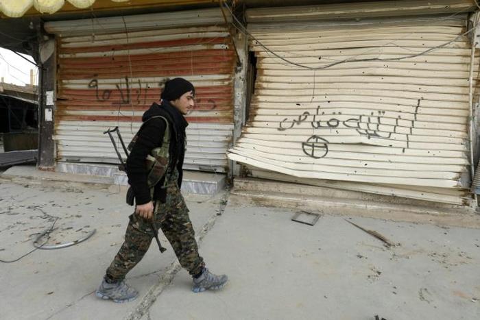 A fighter from the Syrian Democratic Forces (SDF) walks past shops with their fronts painted with the Arabic phrases "beware a sniper" and "caliphate state", in the Syrian town of Hajin on January 27, 2019