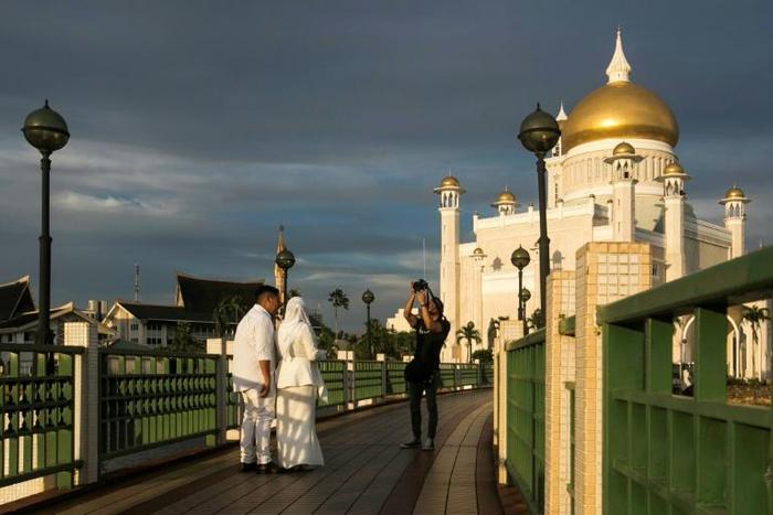 A newlywed couple has their photograph taken at the Sultan Omar Ali Saifuddien mosque in Bandar Seri Begawan, the capital of Brunei, where laws are taking effect that will impose death by stoning for gay sex and adultery
