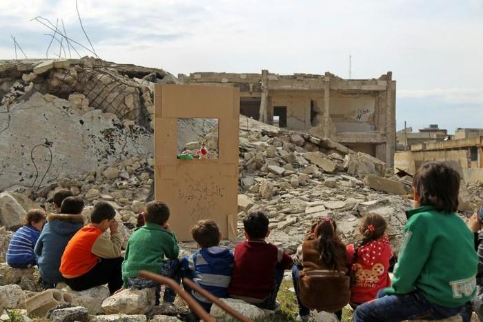 Children watch a puppet show in the ruins of the town of Saraqib in Syria's jihadist-held Idlib region where renewed fighting threatens to flare