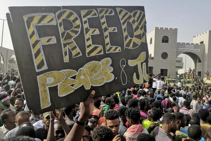 Sudanese anti-regime demonstrators holding up a banner calling for "Freedom, Peace and Justice" around the army headquarters in Khartoum