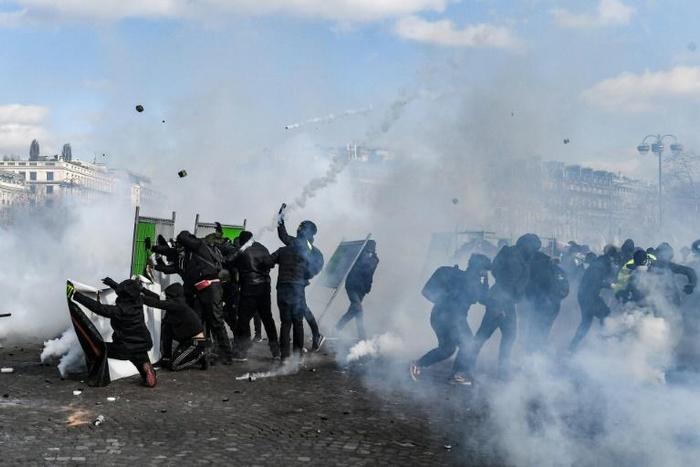 Yellow Vest protesters take shelter behind fences during clashes with riot police forces on the Champs-Elysees