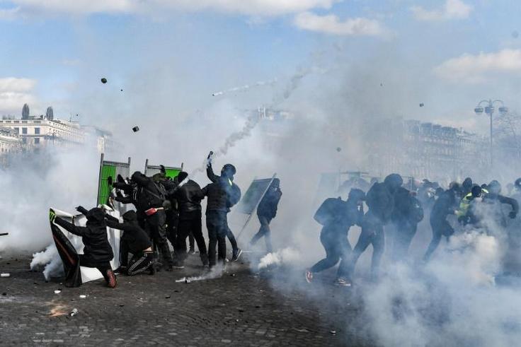 Yellow Vest protesters take shelter behind fences during clashes with riot police forces on the Champs-Elysees