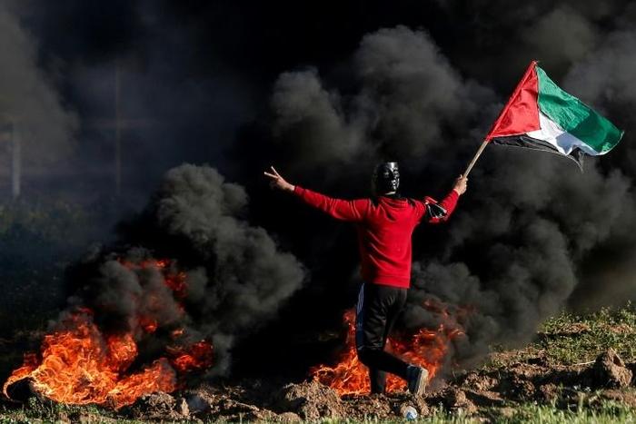 A Palestinian protester waves a flag near burning tyres during clashes with Israeli forces after a demonstration at the border with Israel, east of Gaza City