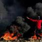 A Palestinian protester waves a flag near burning tyres during clashes with Israeli forces after a demonstration at the border with Israel, east of Gaza City