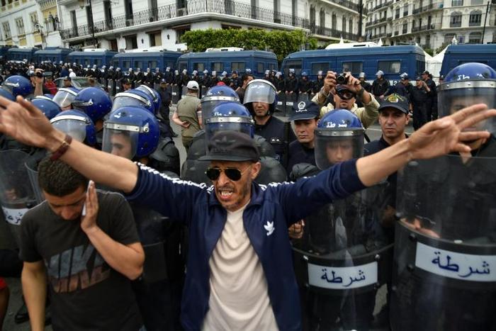 Algerian security forces stand guard behind protesters in the capital Algiers on Friday