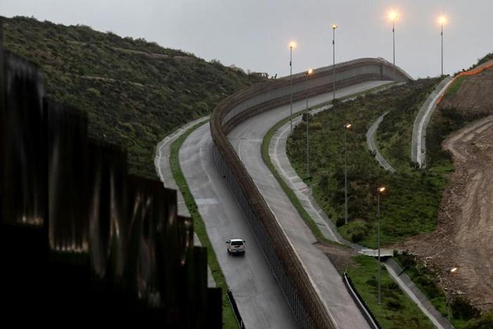 A US Border Patrol vehicle drives near a section of reinforced US-Mexico border fence near Tijuana, Mexico